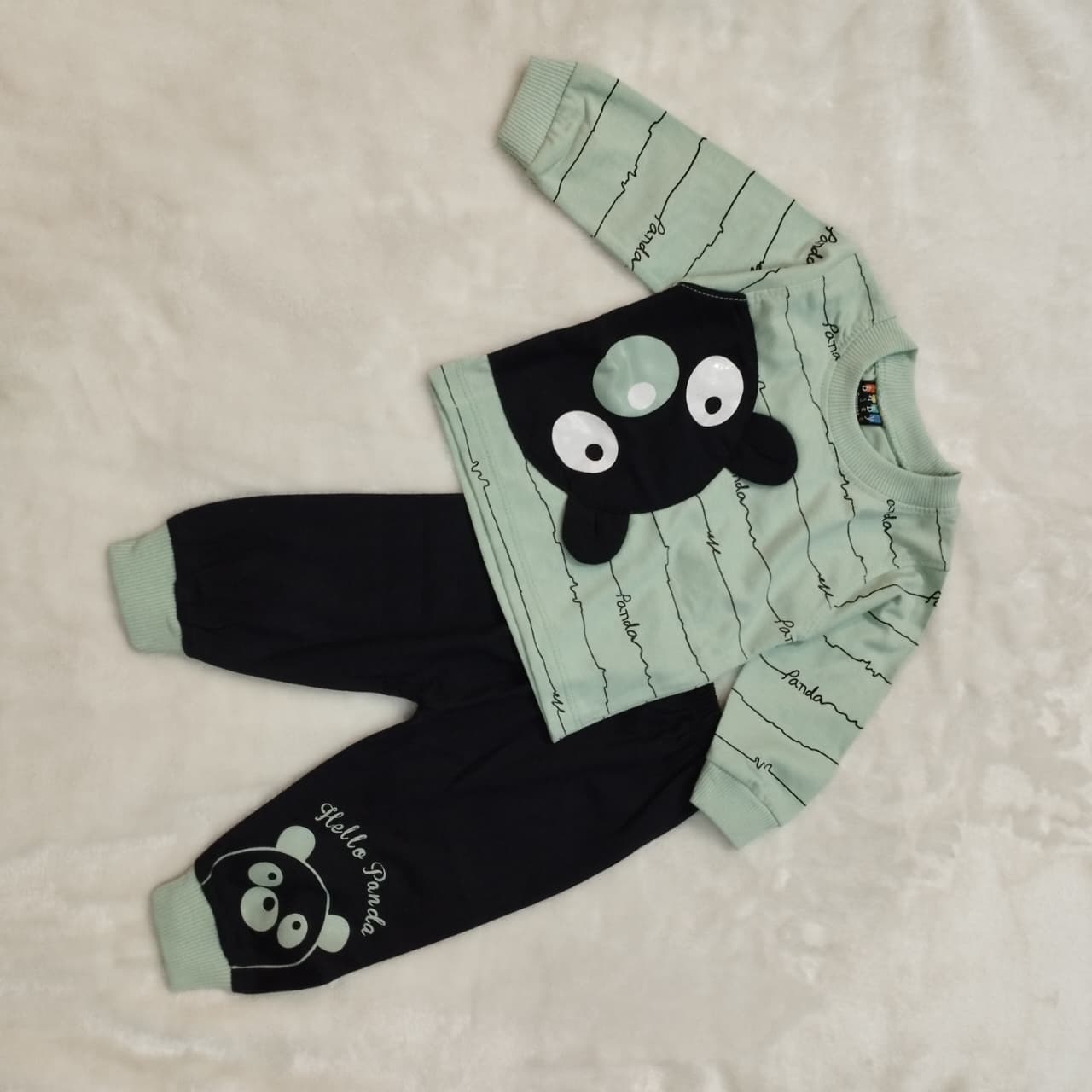 Children's outfit with green top and black pants featuring cartoon face design on a beige background