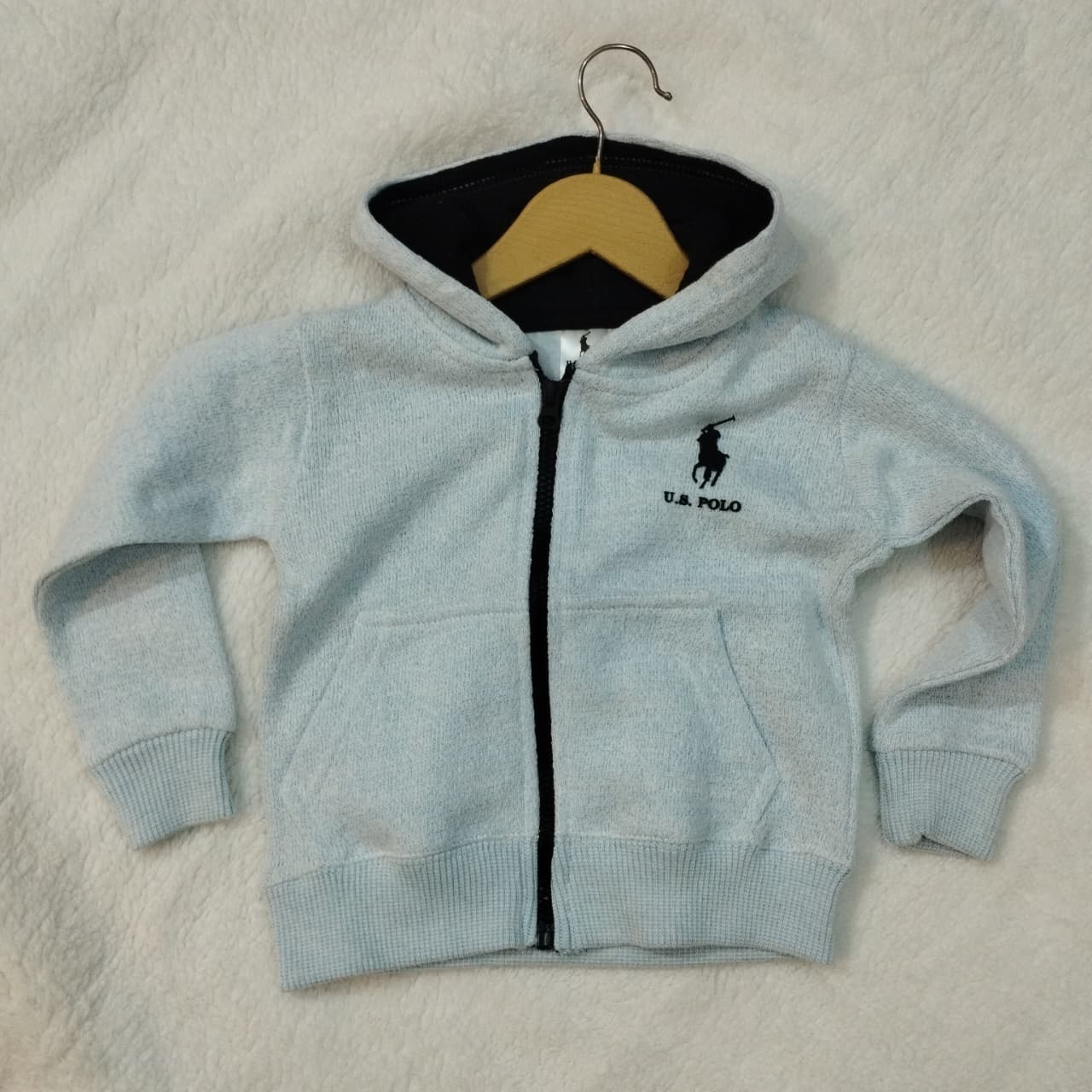 Light blue hoodie with a logo on a beige surface